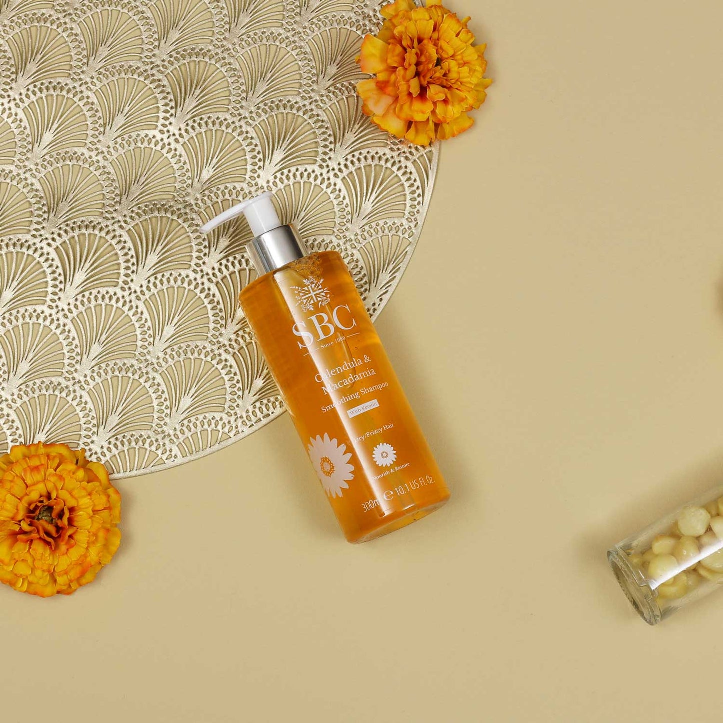 300ml Calendula & Macadamia Shampoo on a beige background with calendula flowers and gold accents
