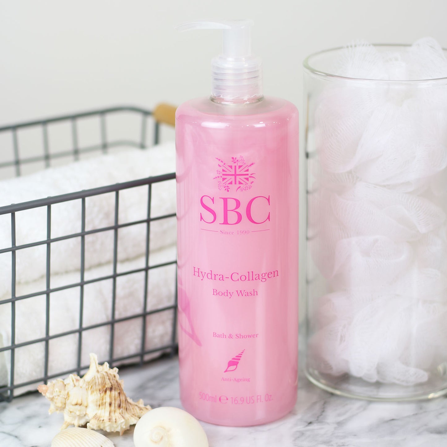 500ml of SBC Skincare's Hydra-Collagen Body Wash on a marble counter with towels and shower scrunchies