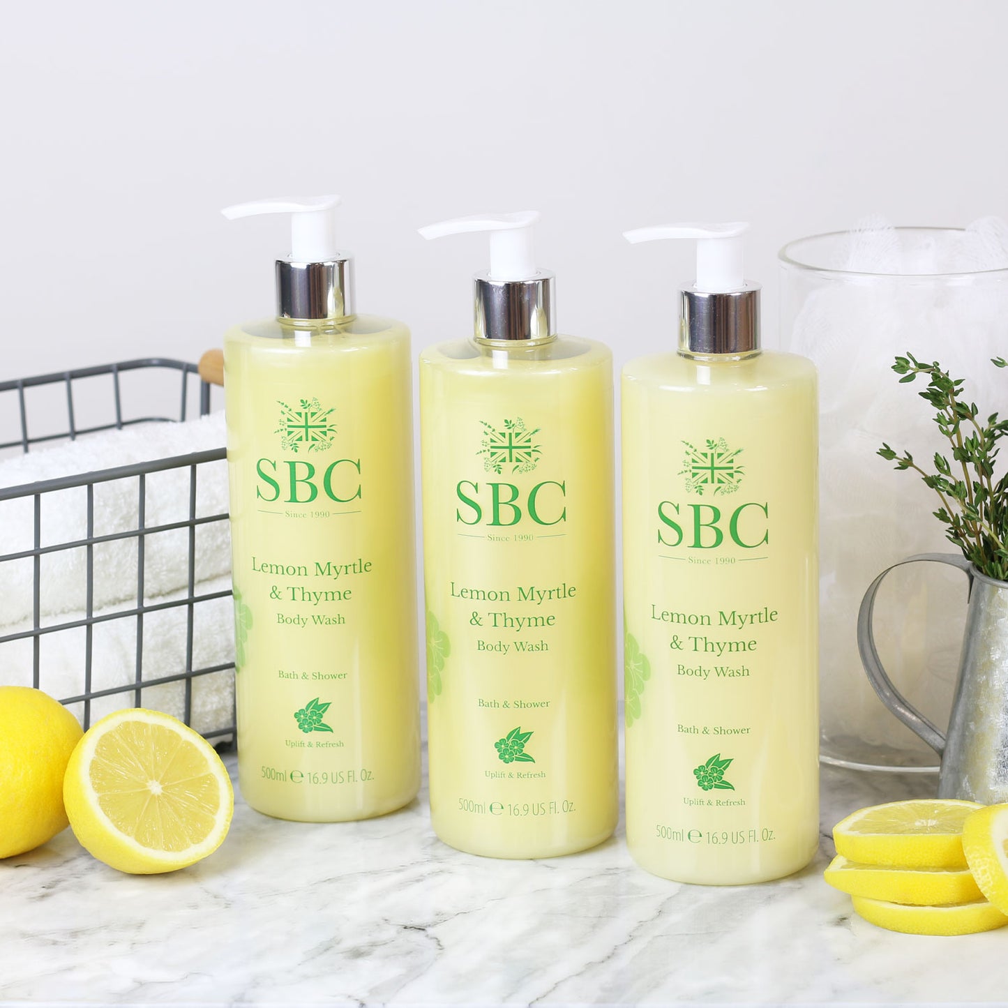 three 500ml Lemon Myrtle & Thyme Body Washes on a marble counter with lemon wedges and white towels