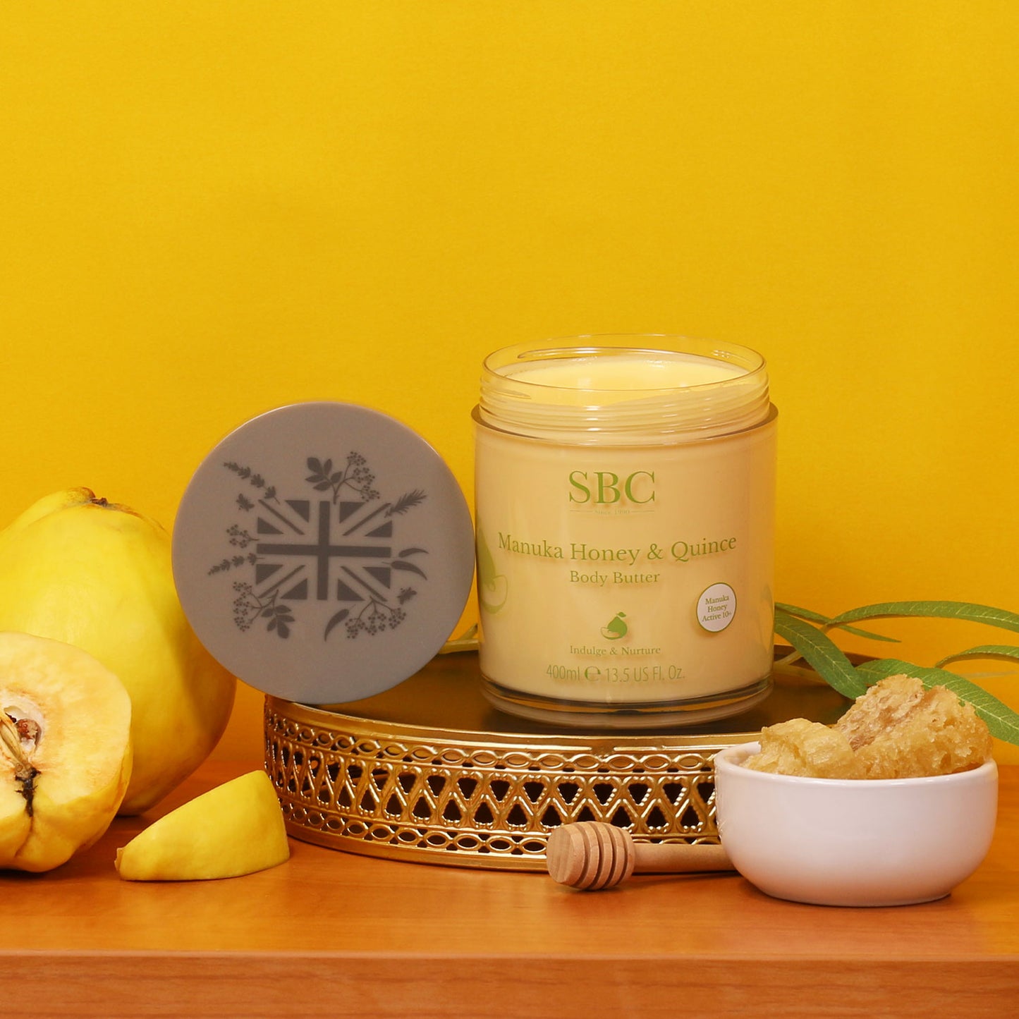 Manuka Honey & Quince Body Butter on a gold plinth with a bright yellow background