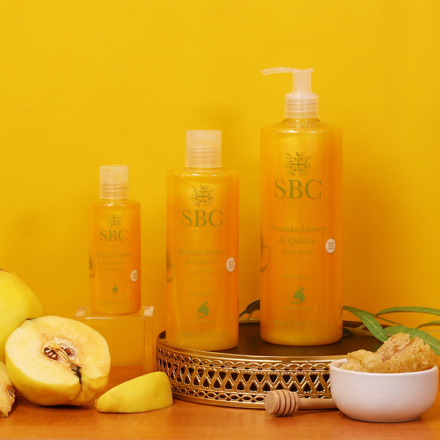 100ml, 300ml and 500ml Manuka Honey & Quince Body Washes on a golf tray with a bright orange background