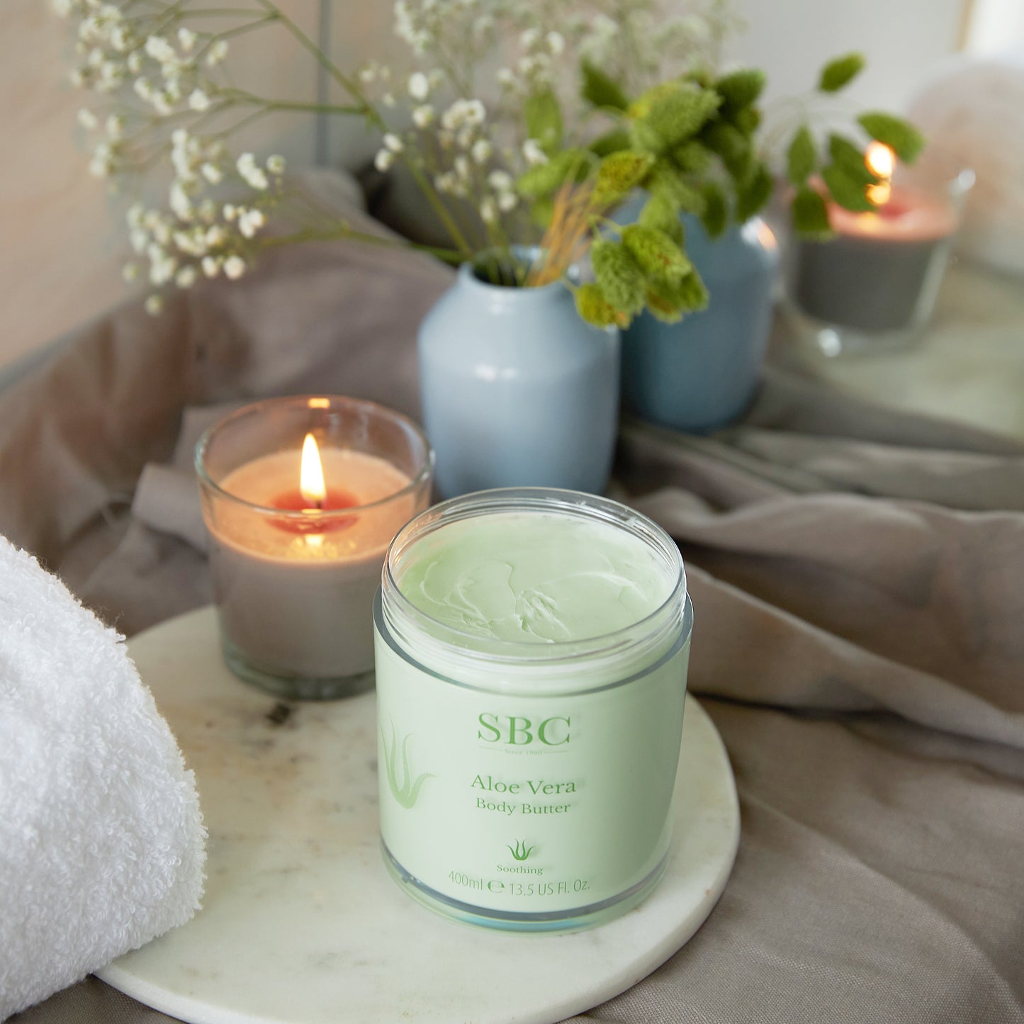 Aloe Vera Body Butter on a bed side table with a candle